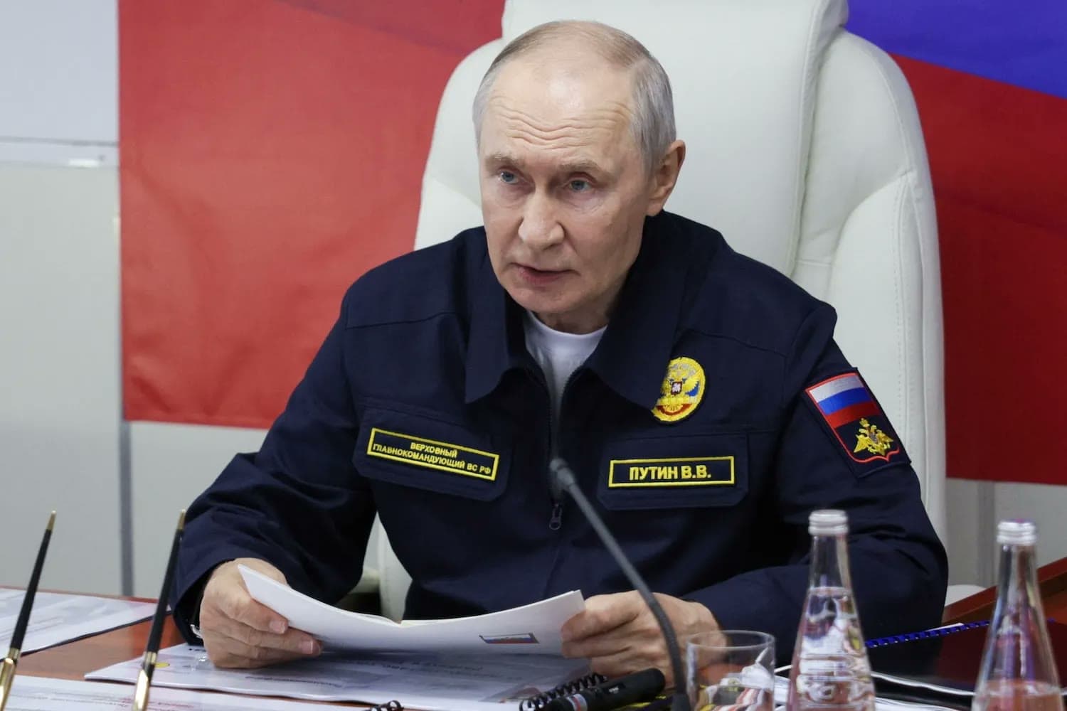 Russian President Vladimir Putin, in a naval uniform, speaks at a table with documents during a military briefing.