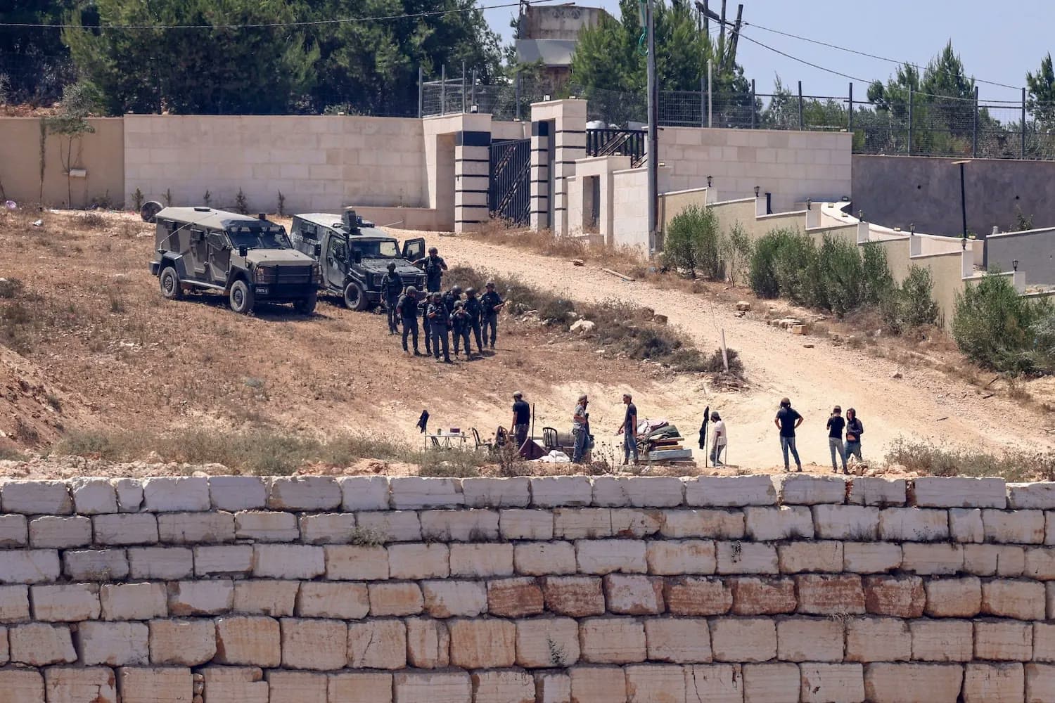 Israeli military vehicles and soldiers stand on a hillside road above a walled Palestinian property in the West Bank village of Qusra.